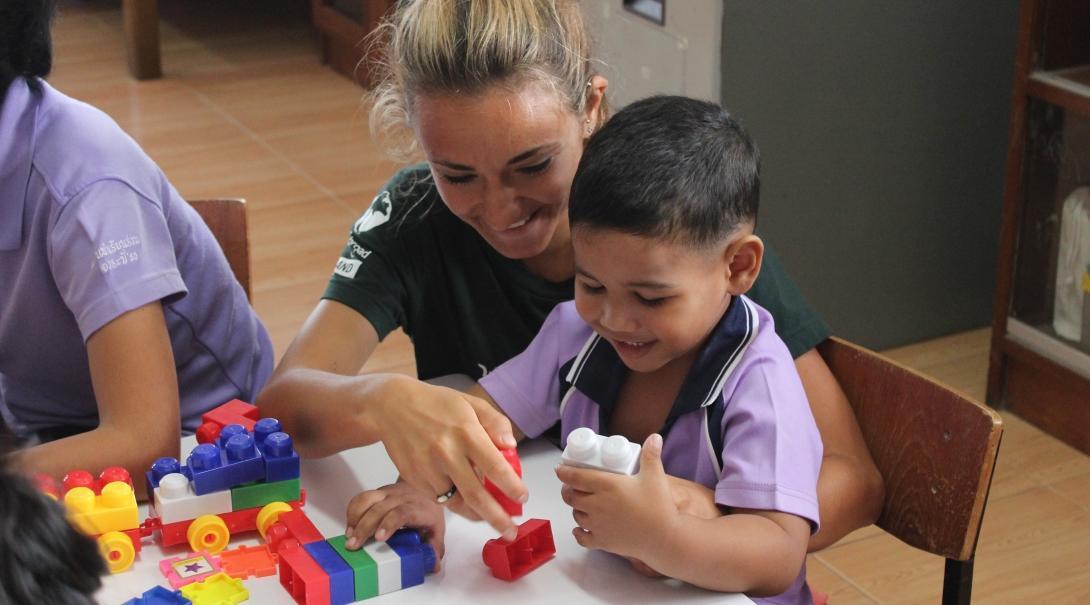Projects Abroad volunteer working with children in Thailand plays lego with young boy during a care placement. Female Childcare volunteer helps young boy build lego blocks in a day care centre during Care placement in Thailand.